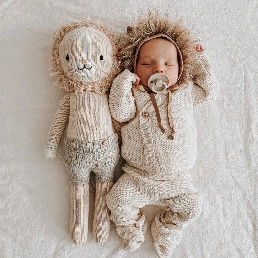 A sleeping baby in a fluffy lion hood, stretched out beside Sawyer the lion.