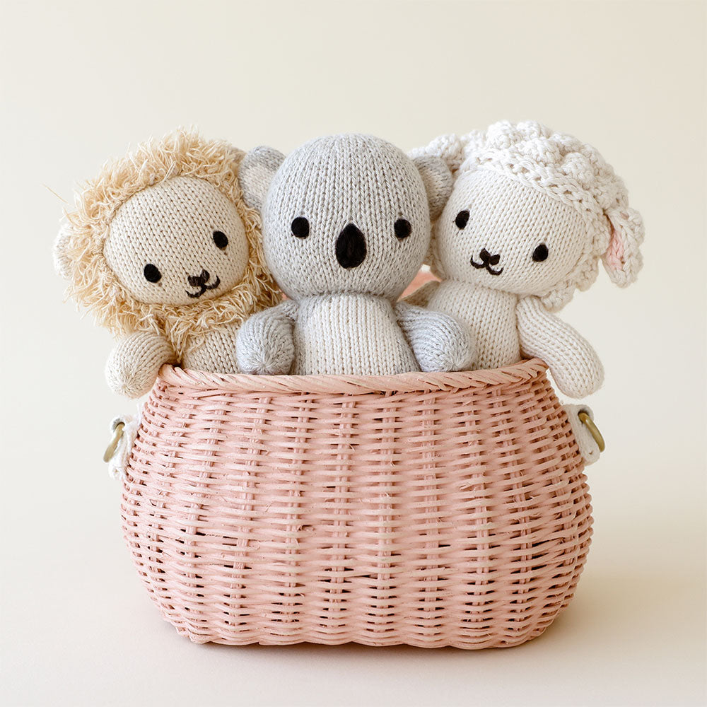 Three baby animal stuffed dolls peeking out of a pink basket: baby lion, baby koala and baby lamb.