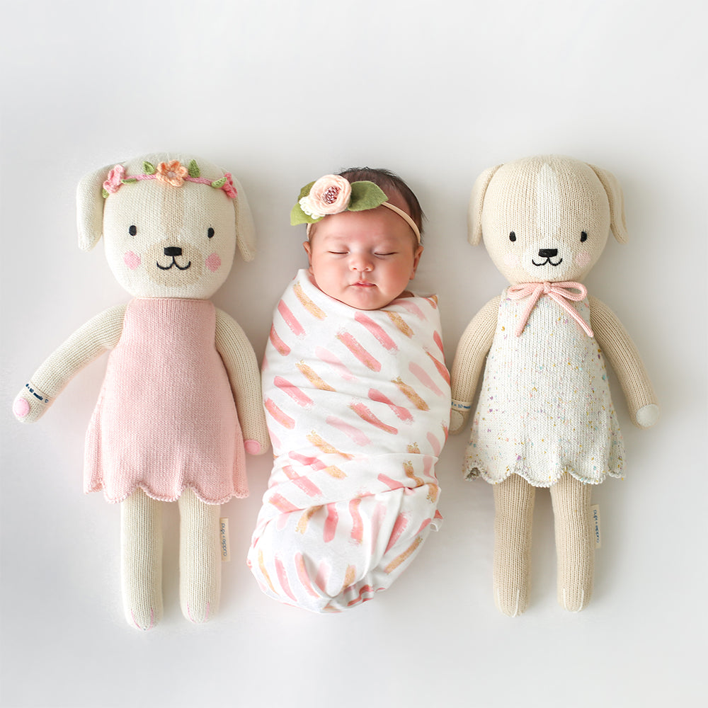 A sleeping baby in between two knit stuffed animals, Charlotte the dog and Mia the dog.