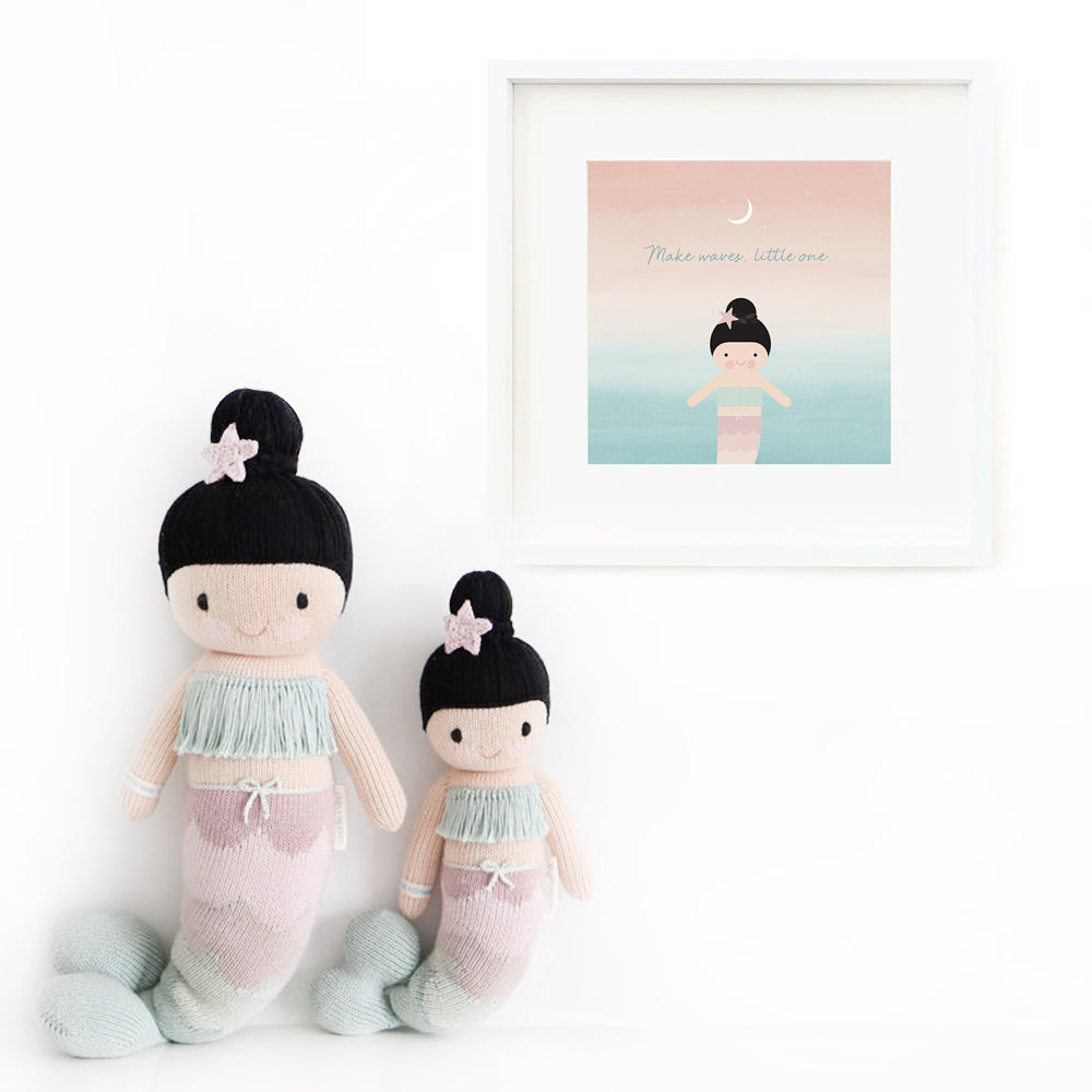 Two Luna the mermaid stuffed animals sitting beside a framed print with a picture of Luna that says “Make waves, little one.”