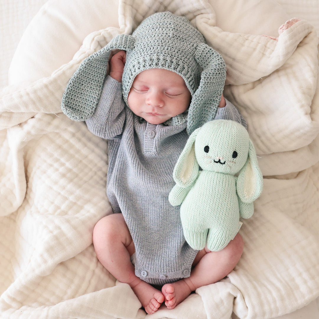 A sleeping baby in a knit, bunny-eared bonnet snuggled next to a baby in mint.