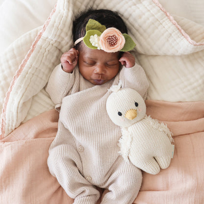 A sleeping baby wearing a felt, floral headband snuggled next to baby gosling.