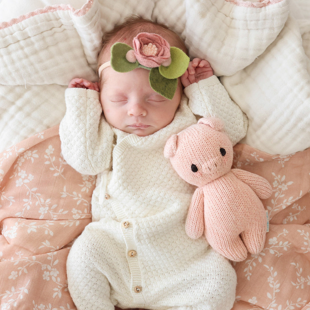 A sleeping baby, wearing a felt floral headband, snuggled next to a baby piglet.