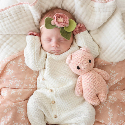 A sleeping baby, wearing a felt floral headband, snuggled next to a baby piglet.