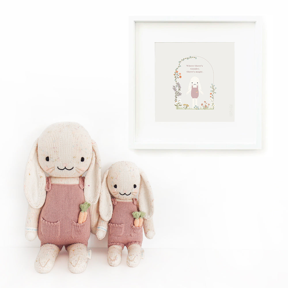 Two Harper the bunny stuffed dolls sitting beside a framed print with a picture of Harper with text that says “Where there's wonder, there's magic".