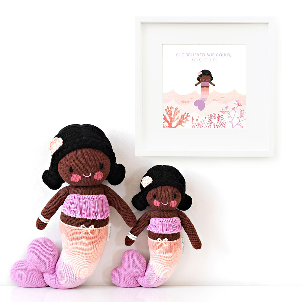 Two Maya the mermaid stuffed animals sitting beside a framed print with a picture of Maya that says “She believed she could, so she did.”