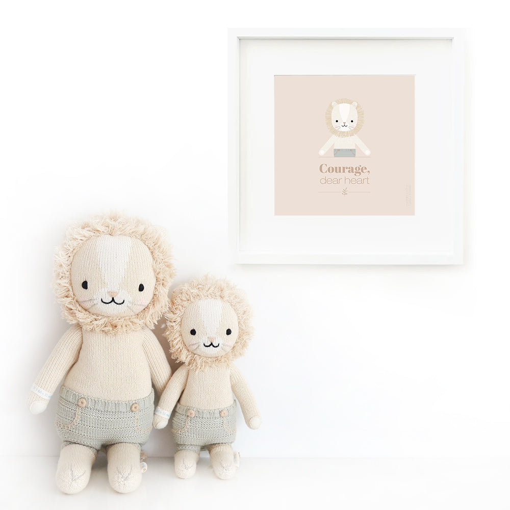 Two Sawyer the lion stuffed animals sitting beside a framed print with a picture of Sawyer that says “Courage, dear heart.”