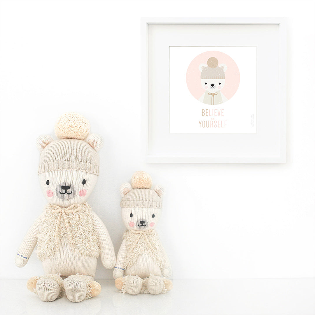 Two Stella the polar bear stuffed animals sitting beside a framed print with a picture of Stella that says “Believe in yourself.”