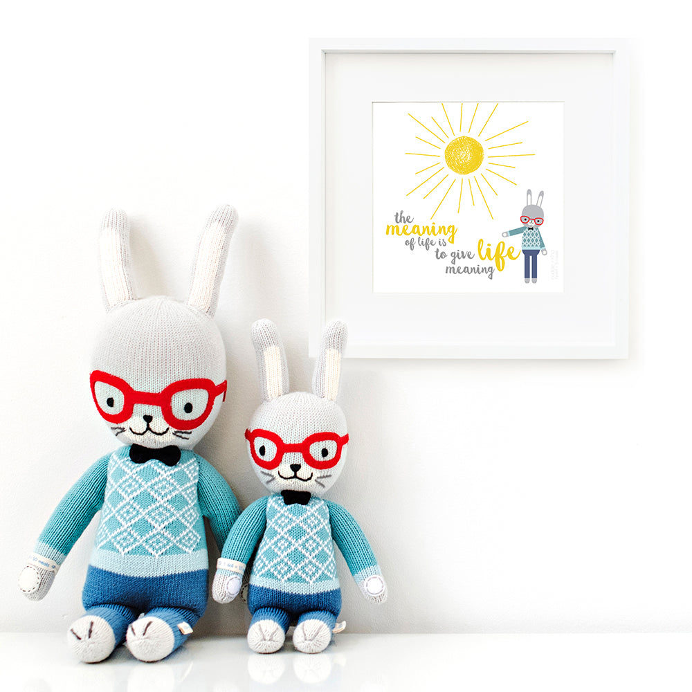 Two Benedict the bunny stuffed animals sitting beside a framed print with a picture of Benedict that says “The meaning of life is to give life meaning.”