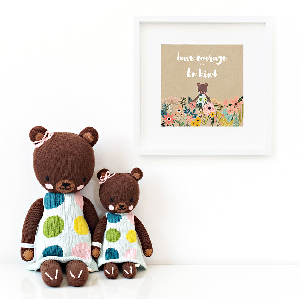 Two Ivy the bear stuffed animals sitting beside a framed print with a picture of Ivy that says “Have courage + be kind.”