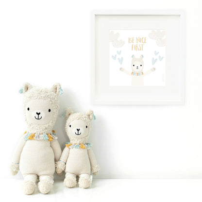 Two Lucas the llama stuffed animals sitting beside a framed print with a picture of Lucas that says “Be nice first.”