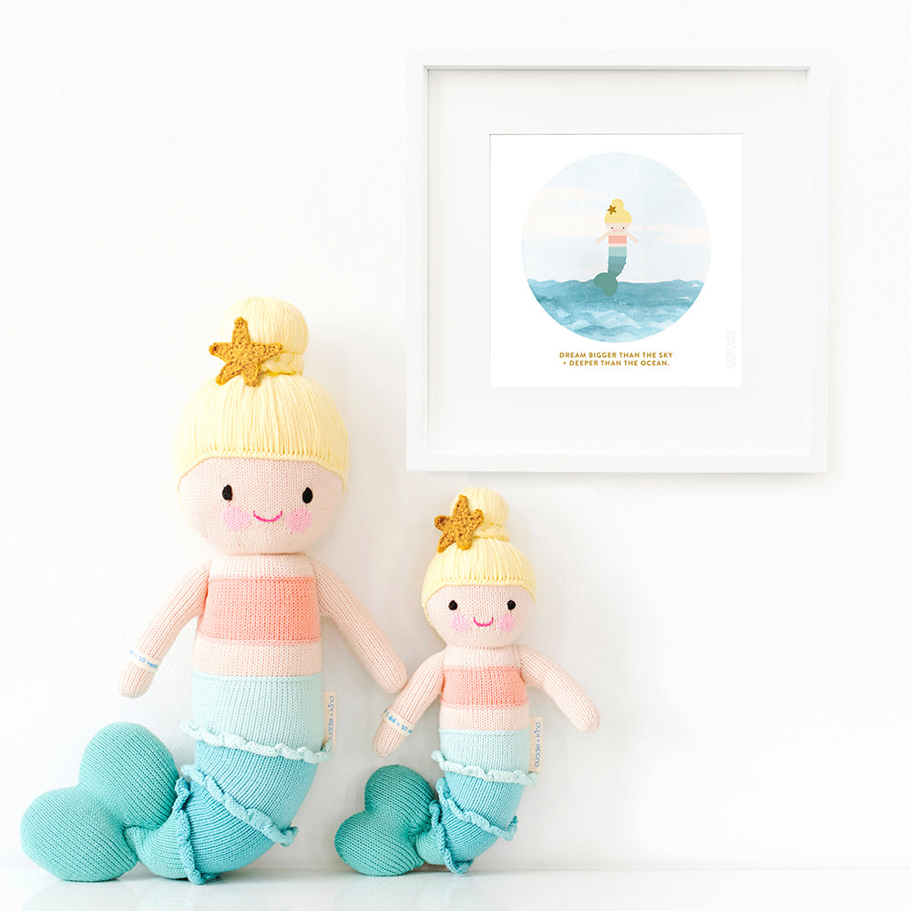 Two Skye the mermaid stuffed dolls sitting beside a framed print with a picture of Skye that says “Dream bigger than the sky + deeper than the ocean.”