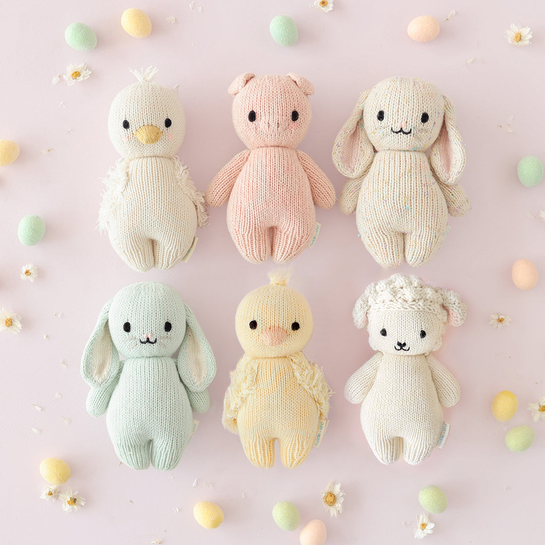 Six baby animal stuffed dolls lying in two rows of 3, surrounded by daisies and pastel Easter eggs.