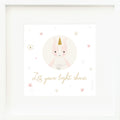 An inspirational print with a graphic of Ella the unicorn on a white background with star accents and the words “Let your light shine” in golden yellow.