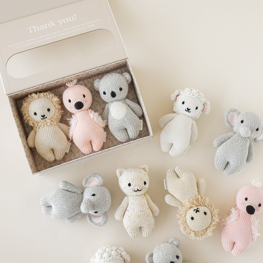 Three baby animals in a baby animal collector’s kit box, next to several other baby animal dolls. The box has text on it that says “Thank you! You’ve just helped make the world a little better for little ones. This collection provides 15 meals to children in need.”