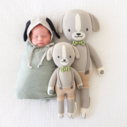 A sleeping baby lying side-by-side with two Noah the dog dolls in the little and regular sizes.