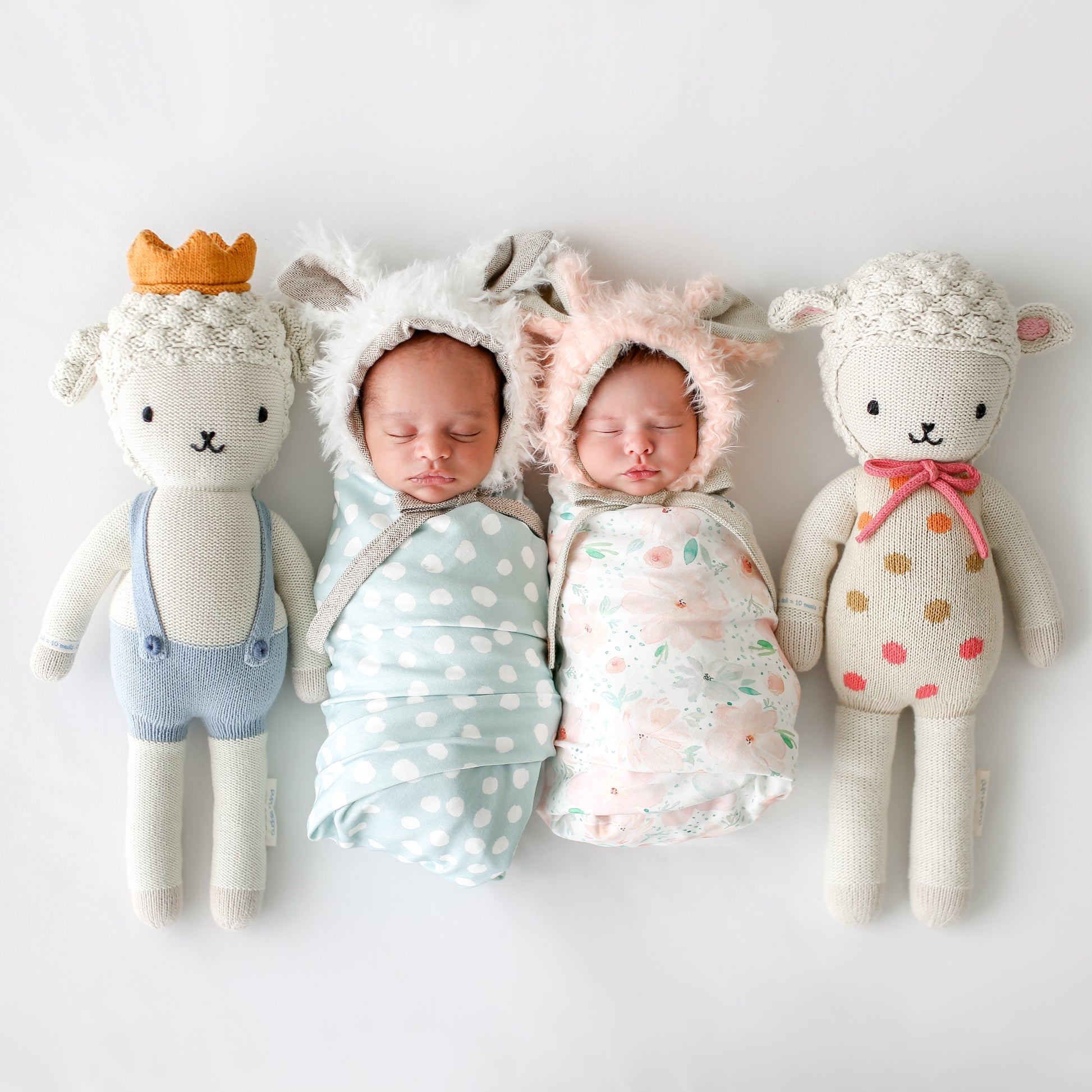 Two sleeping babies snuggled together next to two stuffed lamb dolls: Lucy the lamb and Sebastian the lamb.