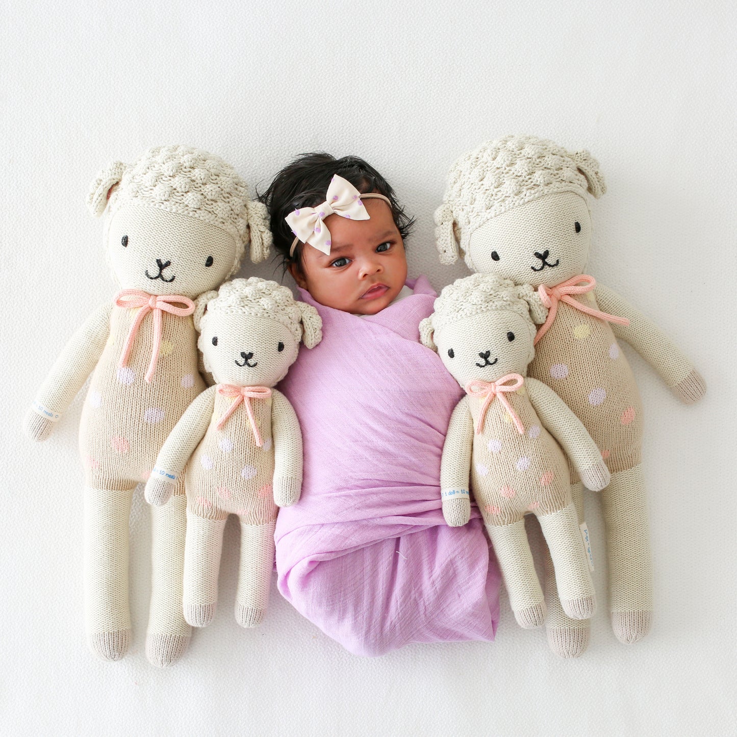 A baby snuggled with four Lucy the lamb dolls in the regular and little sizes.