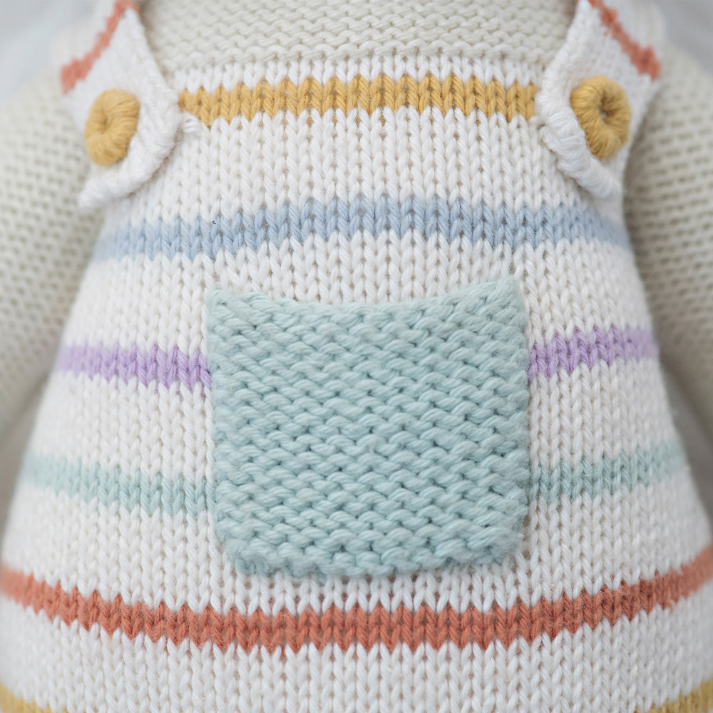 A close-up showing hand-knit details on the overalls an Avery the lamb doll is wearing.