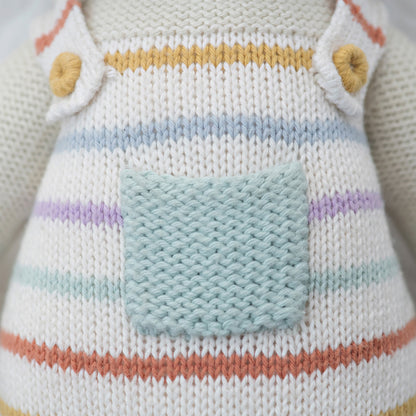 A close-up showing hand-knit details on the overalls an Avery the lamb doll is wearing.