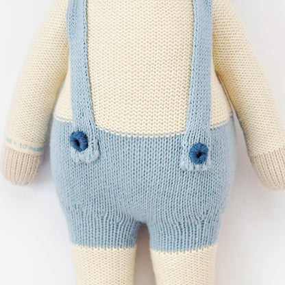 A close-up showing hand-knit details on Sebastian the lamb, including her embroidered yarn buttons on his suspenders.