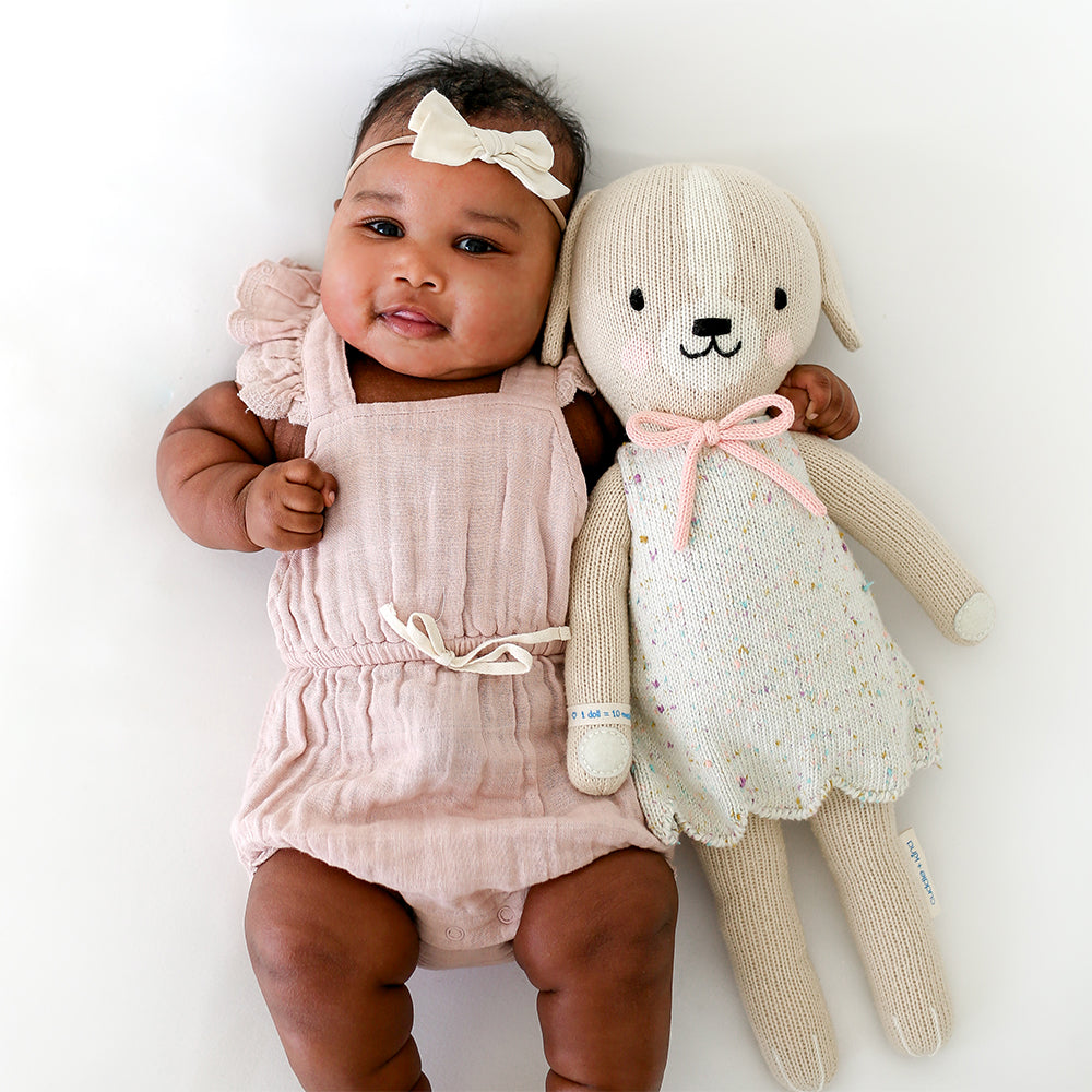 A baby with her arm around a Mia the dog stuffed doll.