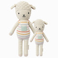 Avery the lamb in the regular and little sizes, shown from the front. Avery is wearing a pair of rainbow striped overalls with a light blue pocket on the front.