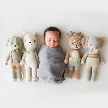 A sleeping baby lying in a row with four hand-knitted dolls: Noah the dog, Lucas the llama, Elliott the fawn and Evan the elephant.