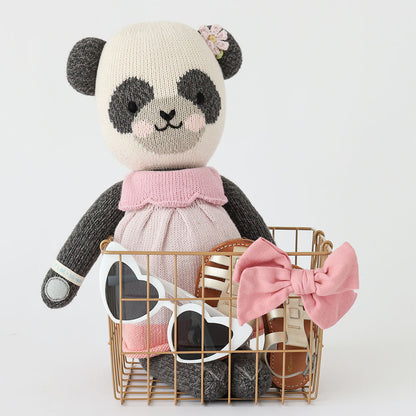 Polly the panda sitting in a wire basket, alongside a pair of children’s sunglasses, sandals and a pink bow-headband.