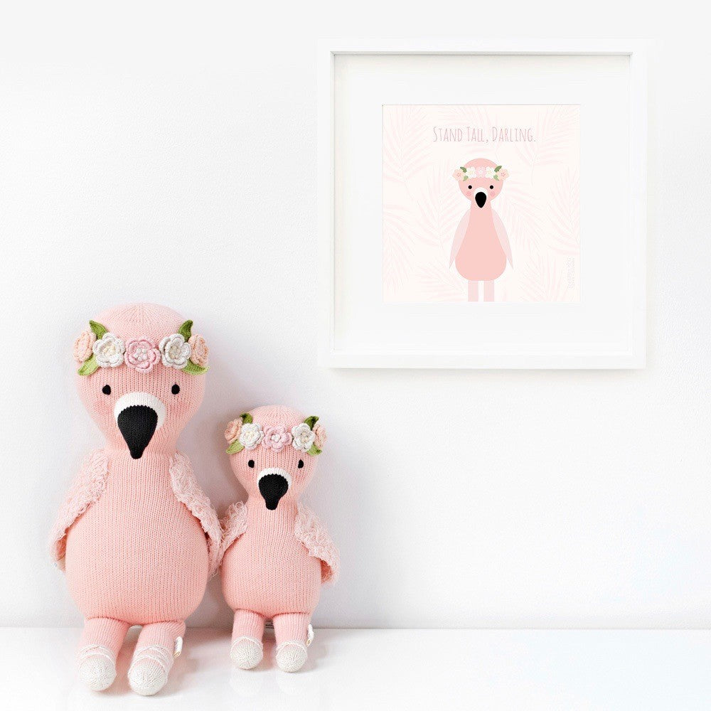 Two Penelope the flamingo stuffed animals sitting beside a framed print with a picture of Penelope that says “Stand tall, darling.”